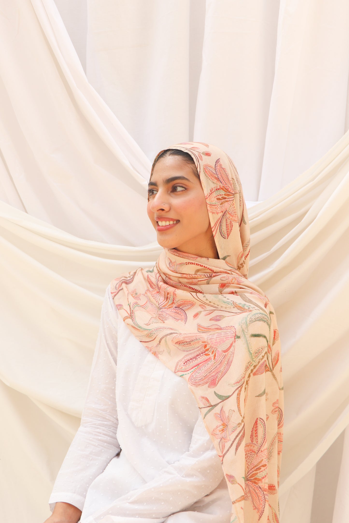 Woman wearing a floral hijab against a white curtain background